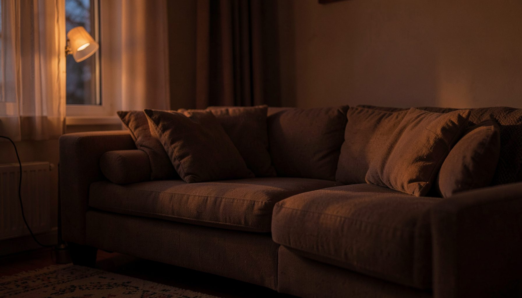 A quiet living room at dusk with soft amber light falling across a sofa, warm and contemplative atmosphere