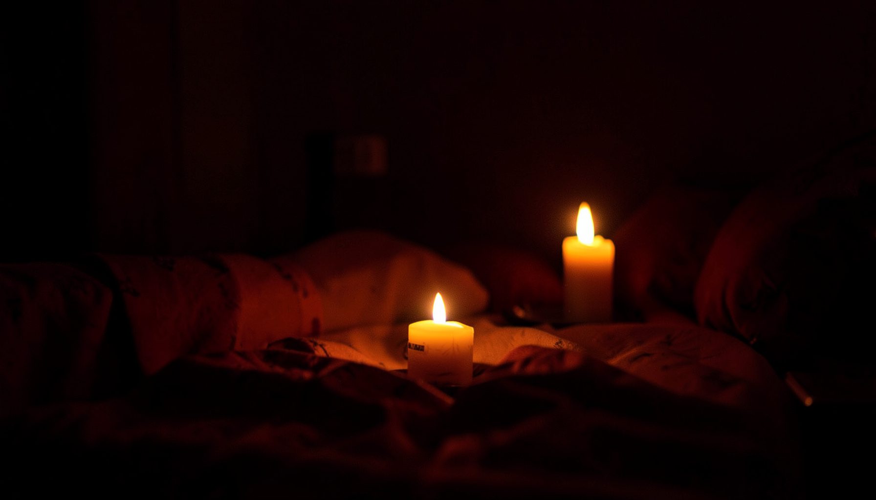 Soft candlelight glow against a dark bedroom, warm amber and deep burgundy tones, intimate and sensual atmosphere